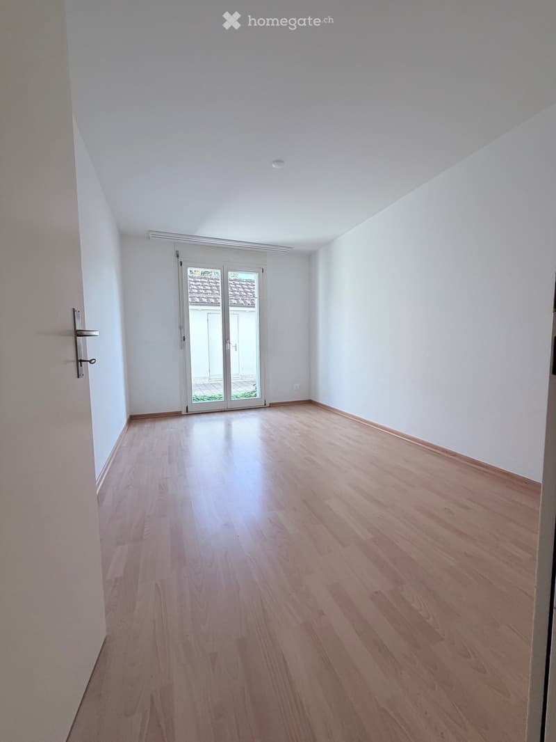 Empty room with light wooden flooring, white walls, and a large sliding glass door leading to an outdoor area.