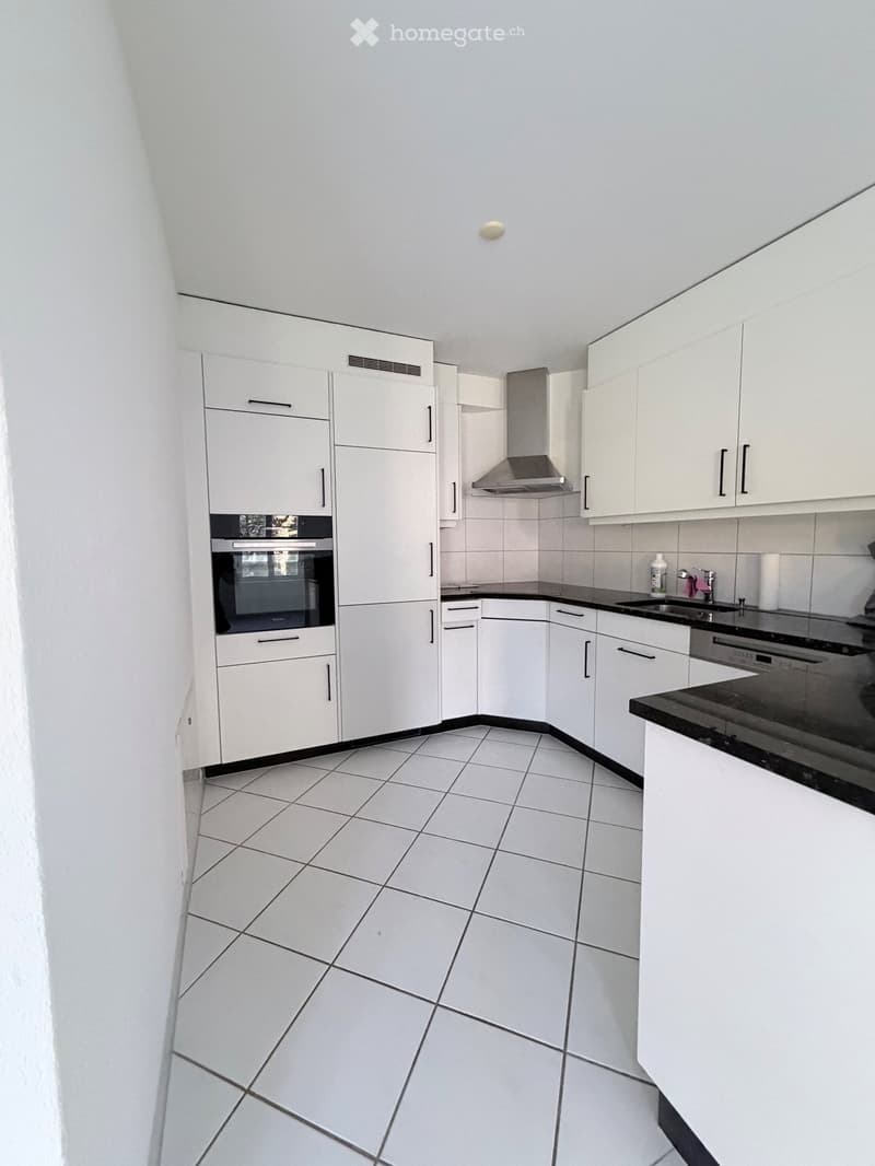 Modern kitchen with white cabinets, black countertops, tiled floor, and stainless steel appliances including an oven, sink, and dishwasher.
