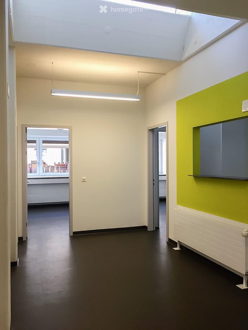 Empty hallway with white walls, black floor, and a green accent wall. Features a hanging light fixture and two open doors leading to other rooms.