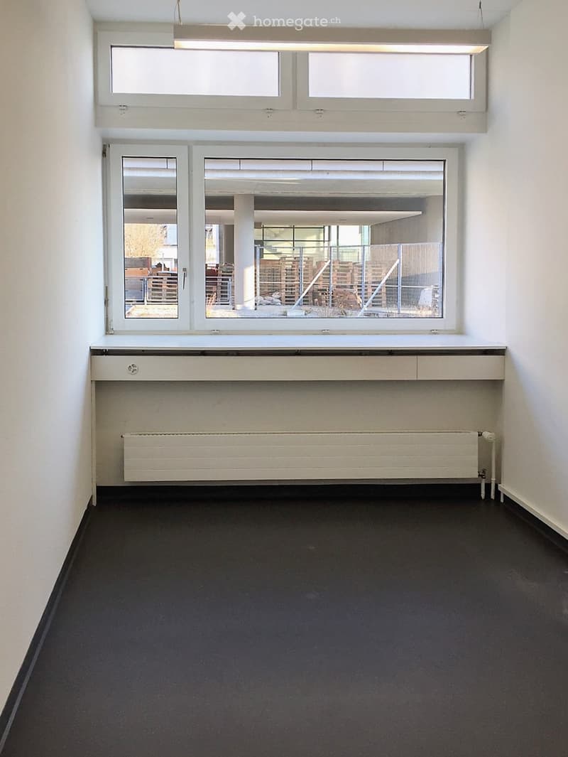 Empty room with white walls, dark carpeted floor, large windows, radiator, and a built-in shelf unit.