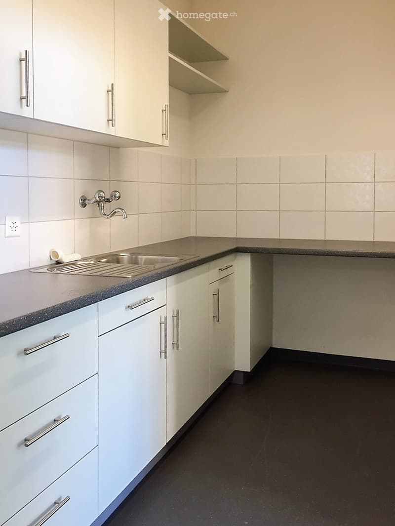 Modern kitchen with white cabinets, stainless steel sink, and dark countertops.