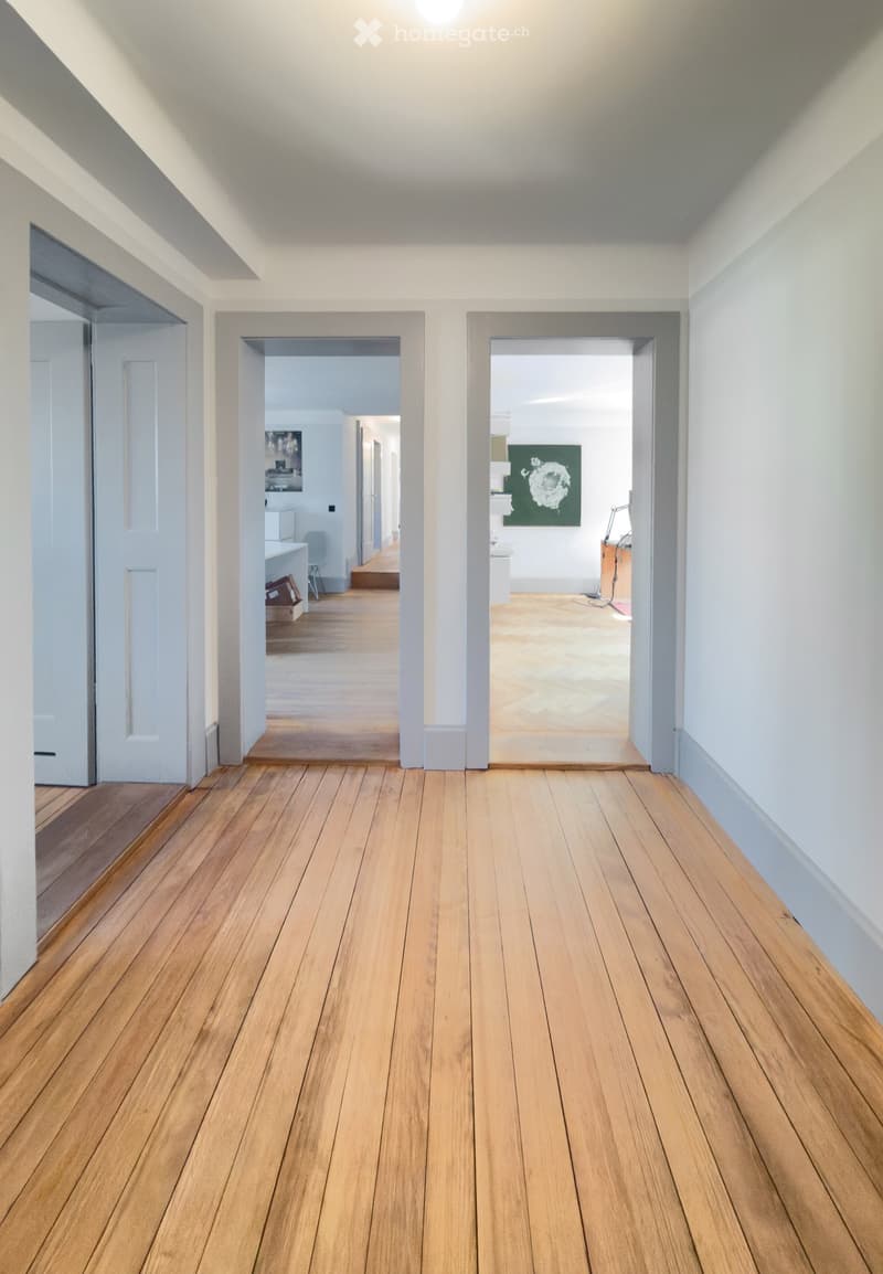 Empty hallway with wooden flooring and white walls, featuring two open doorways leading to adjacent rooms.