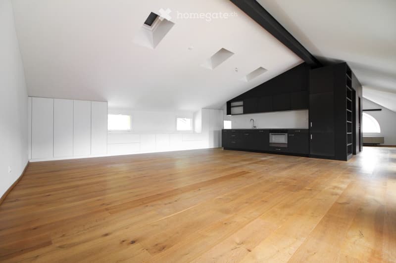 An empty attic space with wooden flooring, white walls, and built-in black cabinets. The room features skylights and large windows, allowing natural light to fill the space.