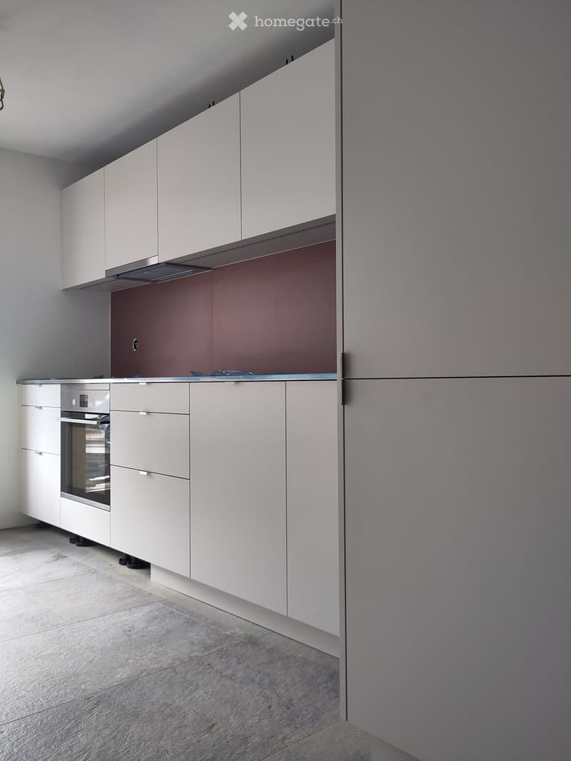 Modern kitchen with white cabinets, stainless steel oven, and a dark backsplash.