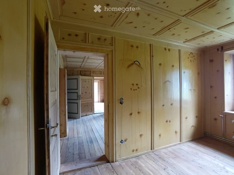Empty hallway with wooden floors, cream-colored walls, and several doors leading to other rooms. Exposed wooden beams on the ceiling and visible wiring.