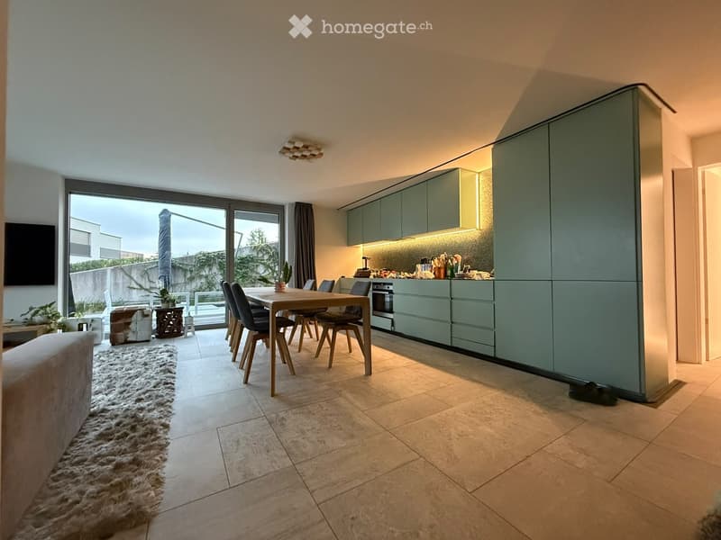 Open-plan living and dining area with a modern kitchen, dining table, chairs, sofa, and a large window with a view.