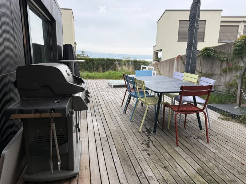 Wooden deck with a grill, table, and colorful chairs, overlooking a scenic view.