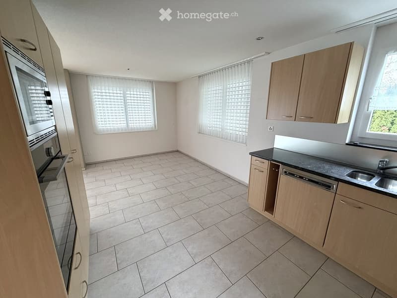 Empty kitchen with light wooden cabinets, tiled floor, and large windows with blinds.