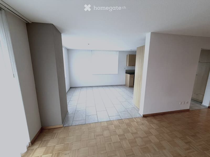 Empty room with wooden flooring and tiled section, white walls, and large windows with blinds. No furniture or equipment present.