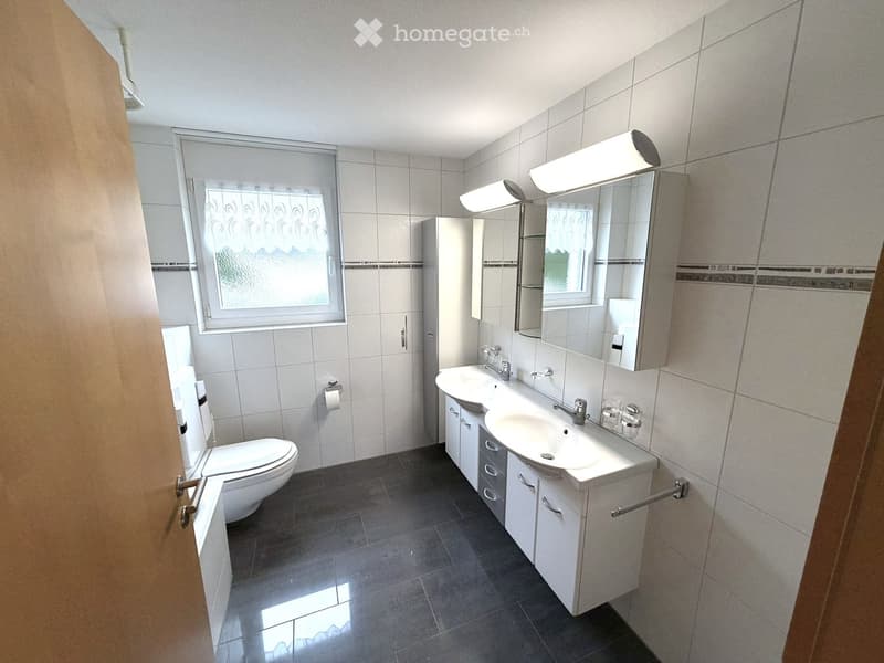 Modern bathroom with white tiles, a double sink vanity, a toilet, and a large mirror with built-in lighting.