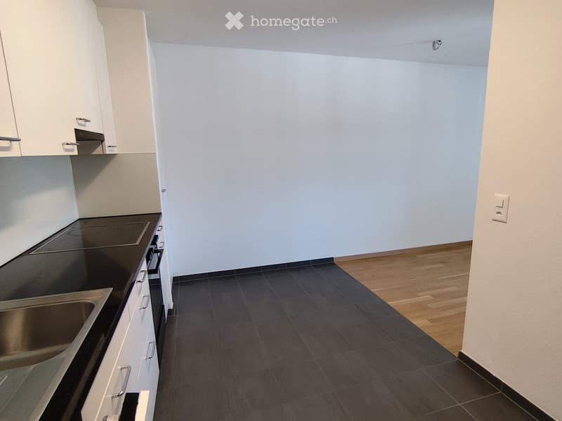 Empty kitchen with white cabinets, dark countertops, and tiled floor. No appliances or furniture present.