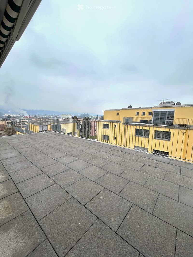 Roof terrace with grey tiled surface, metal railing, and distant cityscape view.