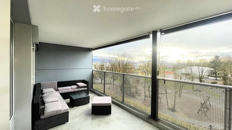 Modern balcony with a view, featuring a black sectional sofa, white cushions, a small glass coffee table, and a white ottoman.