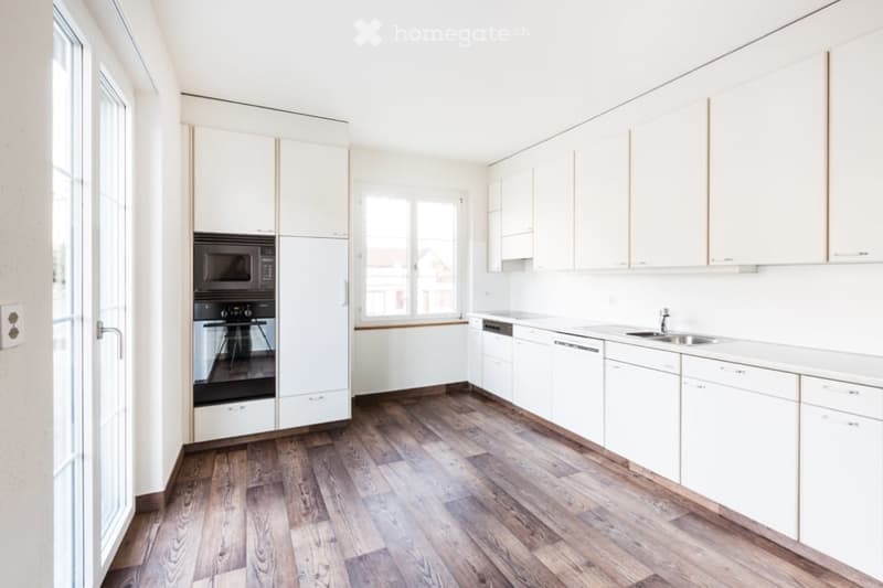 Modern kitchen with white cabinets, wooden flooring, and stainless steel appliances including a microwave, oven, dishwasher, and sink.