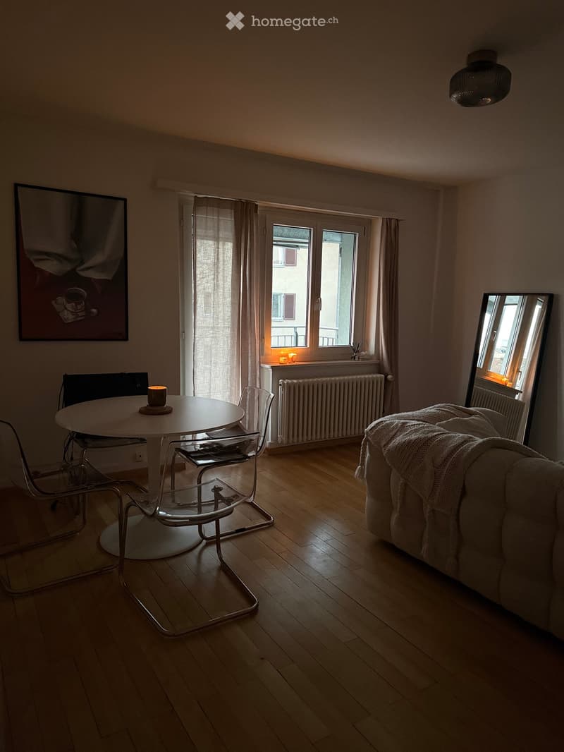 Living room with wooden floor, sofa, round table, chairs, mirror, and picture frame on the wall.