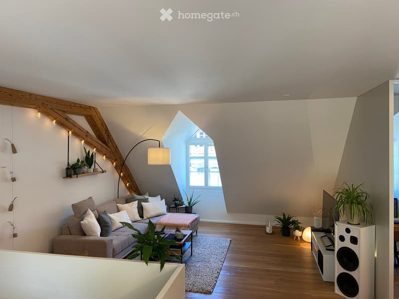 Modern living room with wooden beams, large window, grey sofa, coffee table, floor lamp, speaker, and potted plants.