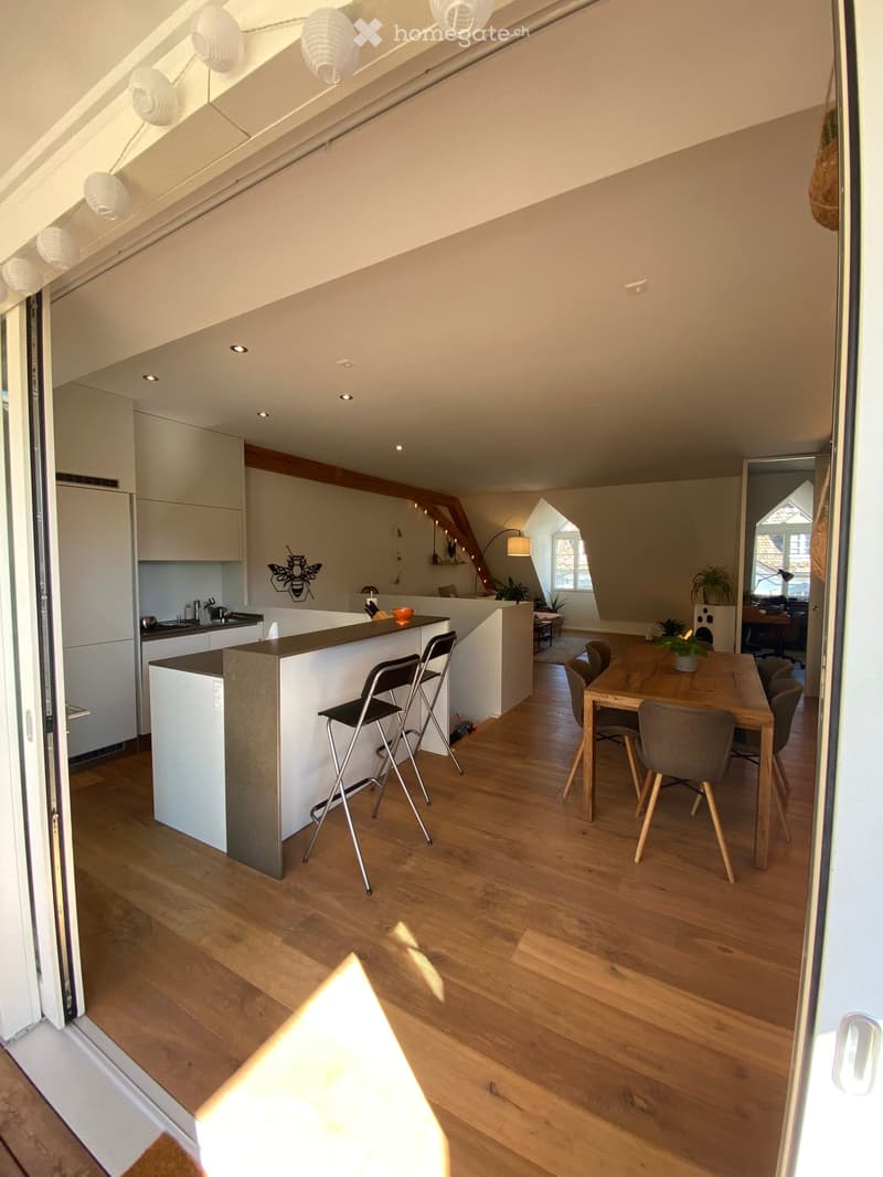 Open-plan kitchen and dining area with light wood flooring, white cabinets, a kitchen island with bar stools, and a dining table with chairs.