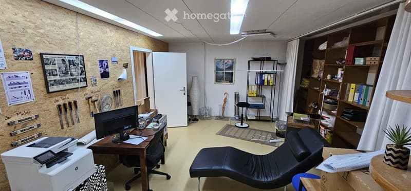 Office space with a wooden desk, computer screen, office chair, printer, shelves, and a lounge chair.
