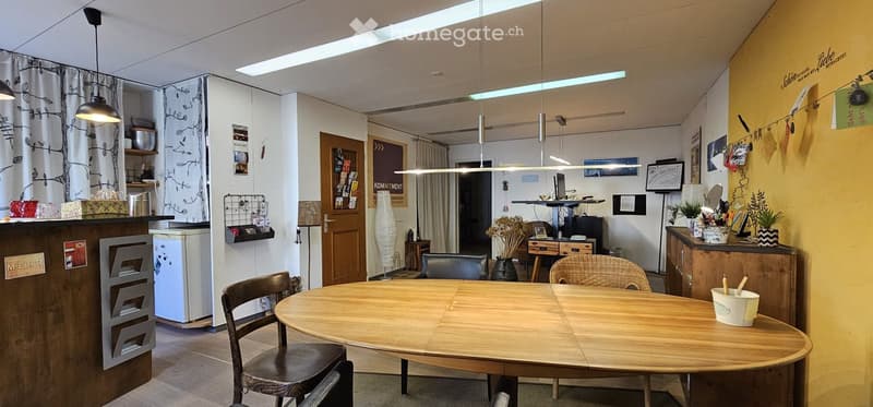 A modern, well-lit room with a round wooden table and chairs, a refrigerator, a screen, and decorative elements like plants and lamps.