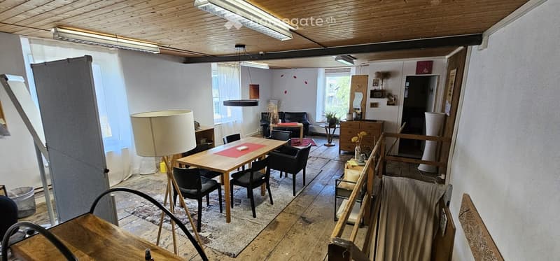 Open-plan living and dining area with wooden floors, a dining table with chairs, a sofa, a lamp, and a cabinet with a mirror.