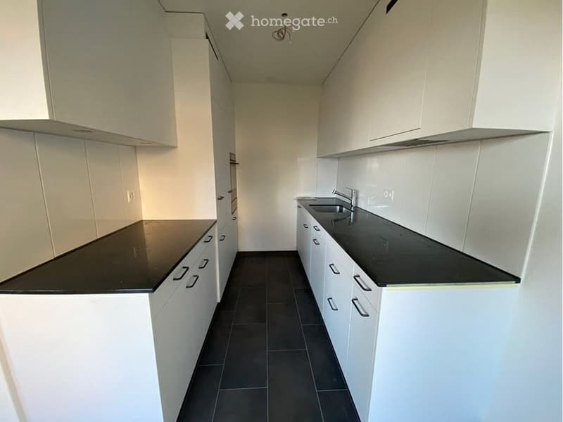Empty kitchen with white cabinets, black countertops, and dark tiled flooring.