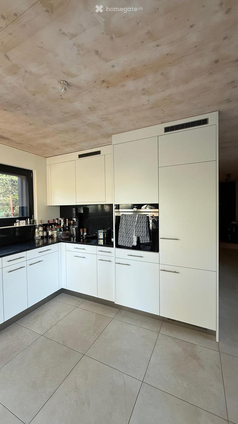 Modern kitchen with white cabinets, stainless steel appliances, and a black countertop. The ceiling features a wooden panel design, and the floor is tiled.