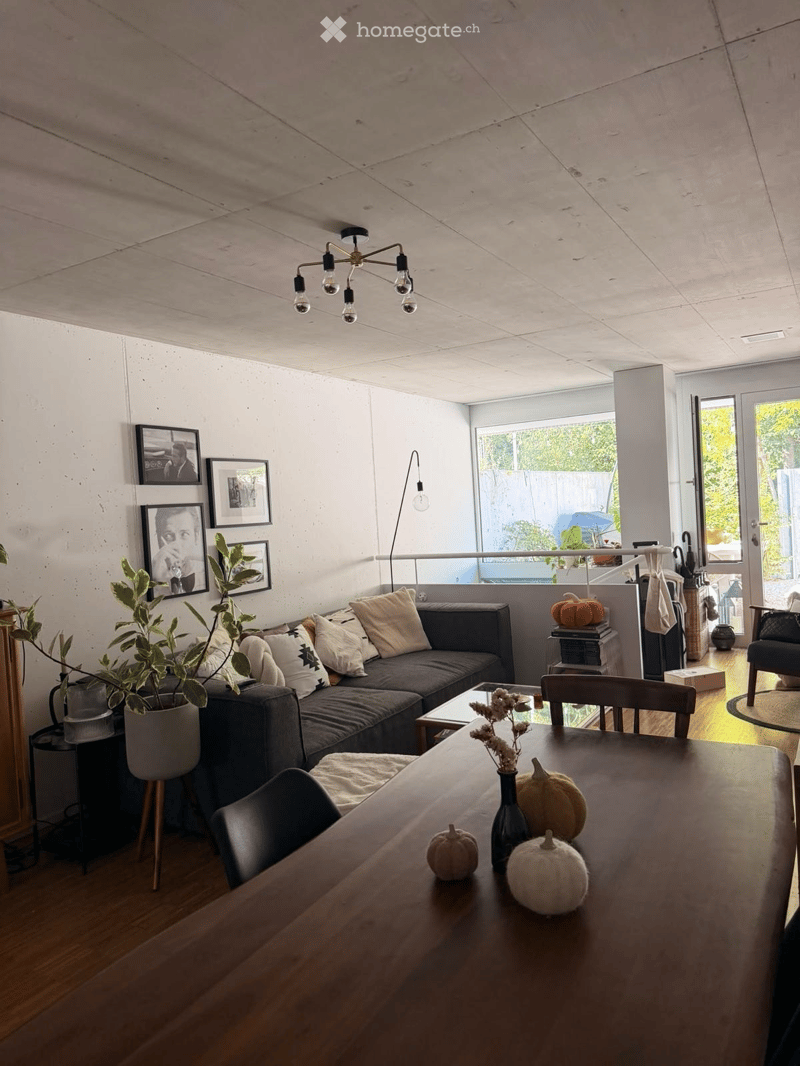 Living room with a grey sectional sofa, coffee table, dining table with chairs, decorative pumpkins, potted plant, picture frames, and a floor lamp.