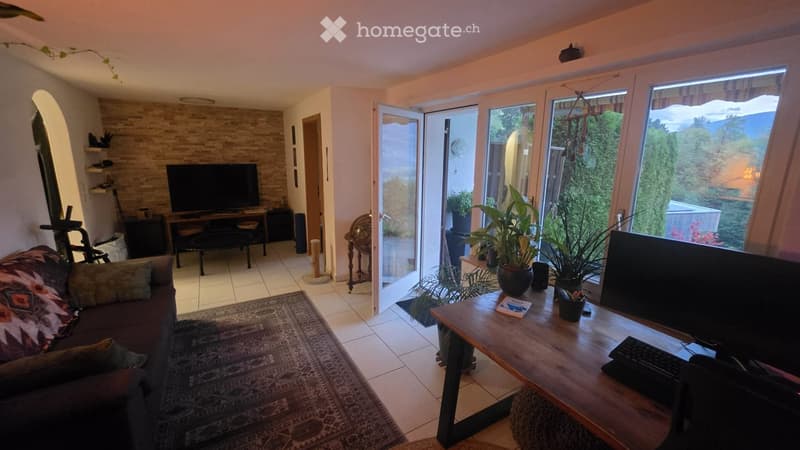 Bright living room with large windows offering a scenic view, featuring a sofa, coffee table, television, and plants.