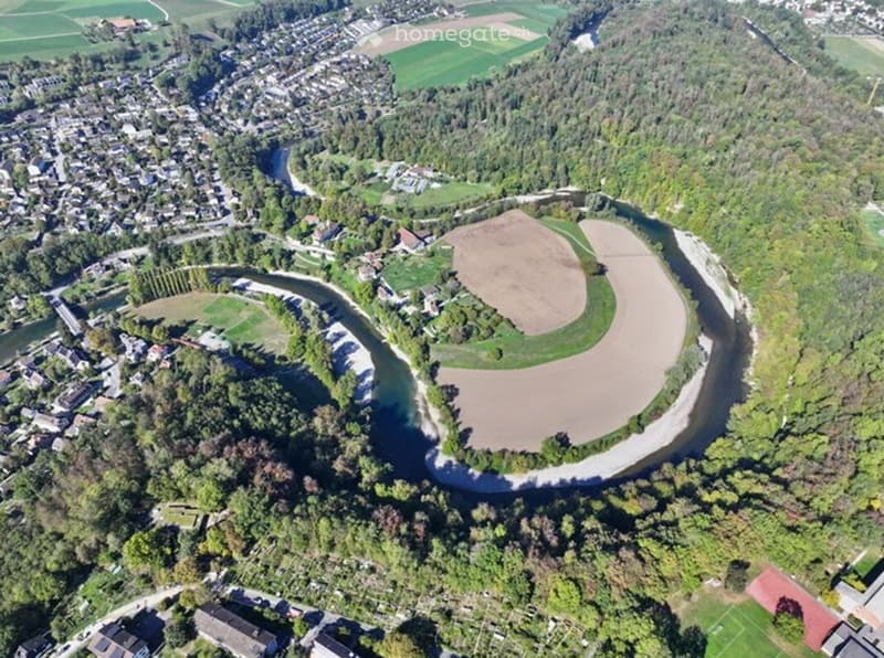 Aerial view of a rural area with a river winding through, surrounded by green fields, trees, and scattered buildings.