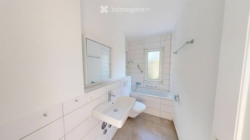 Modern bathroom with white tiles, a sink, toilet, bathtub, and a large mirror above the sink.