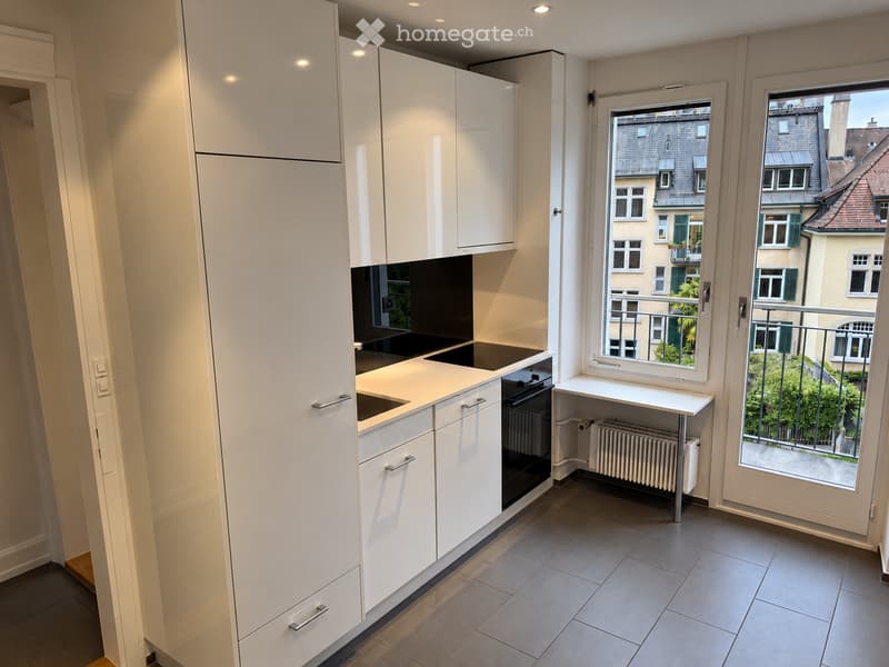Modern kitchen with white cabinets, a sink, an oven, and a small table near the window offering a city view.