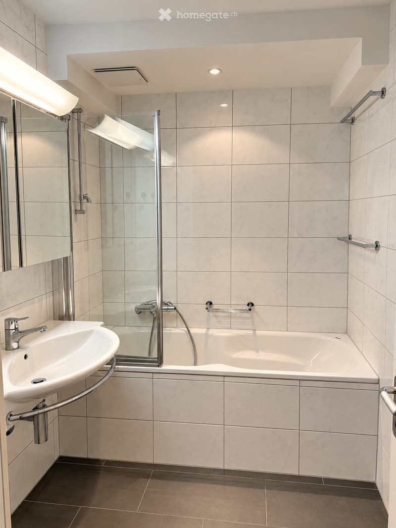 Modern bathroom with marble tiles, a white sink with a chrome faucet, a bathtub with a glass shower enclosure, and built-in shelves.