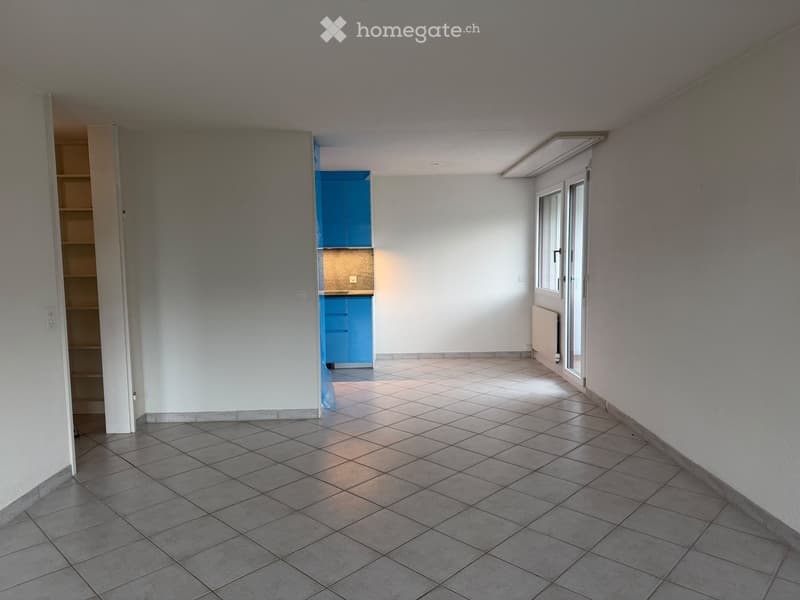 Empty room with tiled floor, white walls, and a small blue cabinet visible in the background.