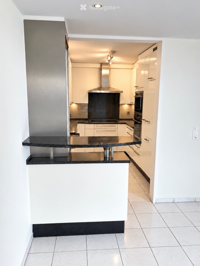 Modern kitchen with white cabinets, black countertops, a central island, and stainless steel appliances including a stove, oven, and range hood.