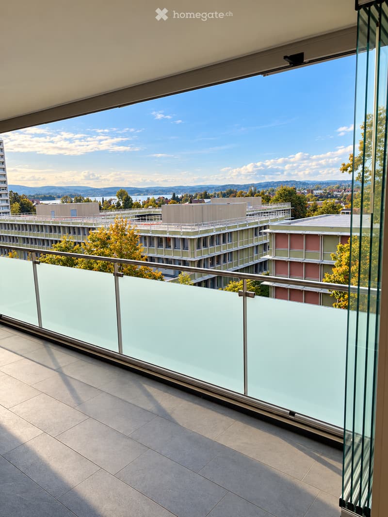 Modern balcony with glass railing, tiled floor, and expansive view of cityscape and surrounding landscape.