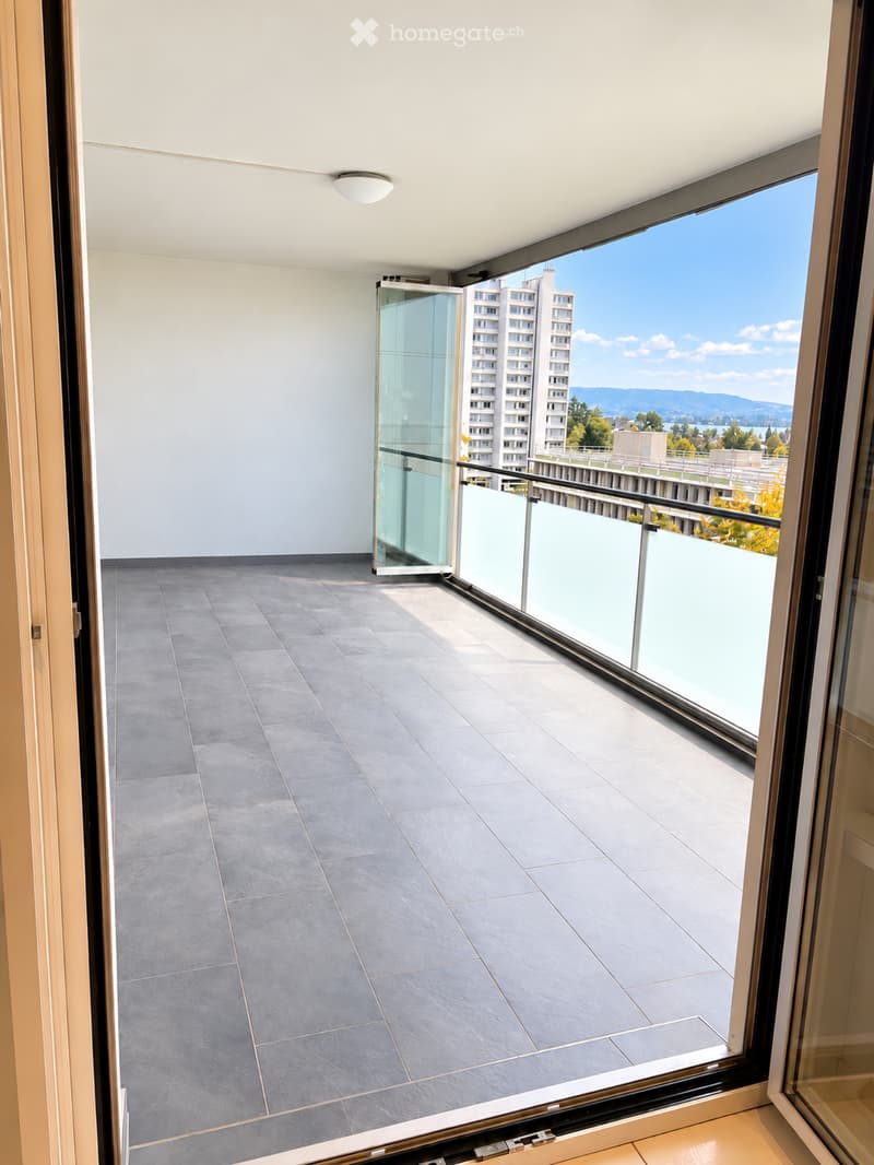 Modern balcony with grey tiled flooring, glass balustrade, and expansive city view.