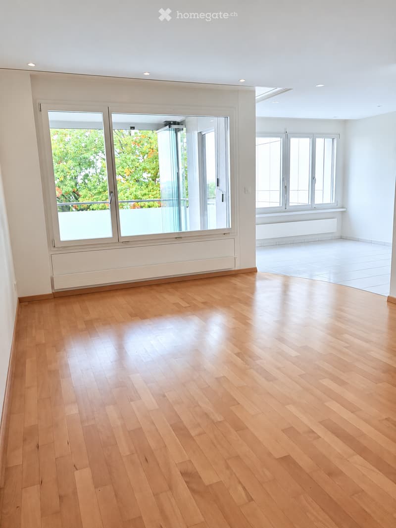 Empty room with light wooden flooring, white walls, large windows, and a sliding glass door leading to a balcony.