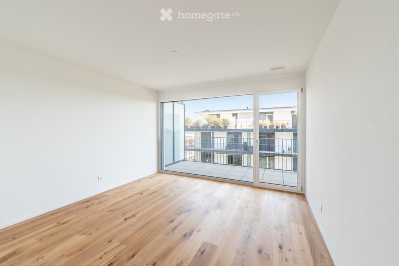 Empty room with light wooden flooring, white walls, and large glass sliding doors leading to a balcony.