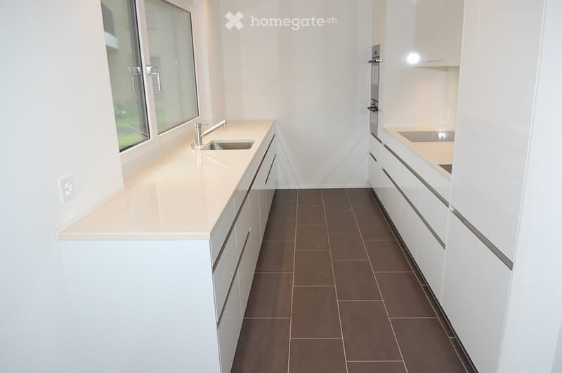 Modern kitchen with white cabinets, beige countertops, and a brown tiled floor. Features a sink with a modern faucet and built-in cabinets.
