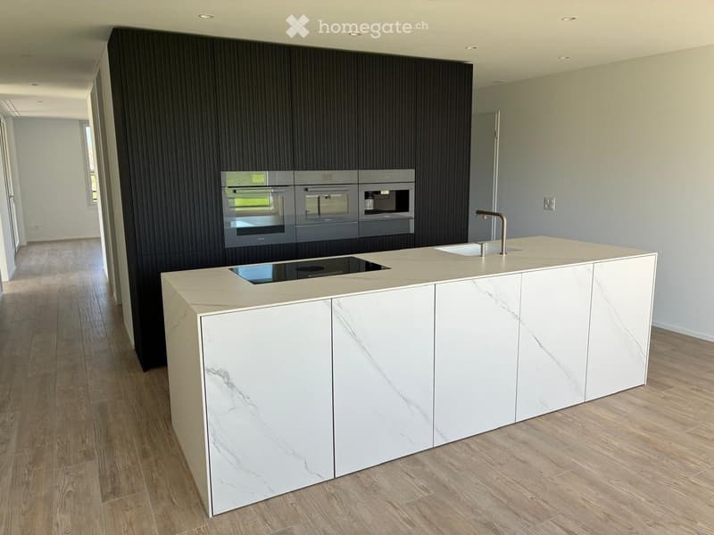 Modern kitchen with a white marble island, built-in ovens, and a sleek faucet.