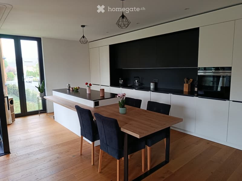 Modern kitchen with white cabinets, dark countertops, a central island, and a dining area with a wooden table and chairs.