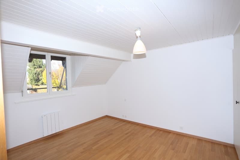 Empty room with white walls, wooden floor, large windows, and a hanging light fixture.