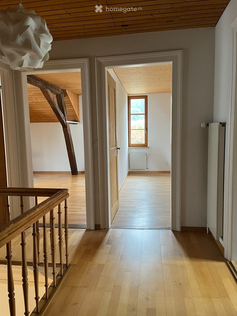 Spacious hallway with wooden flooring, wooden staircase railing, and a small window at the end.