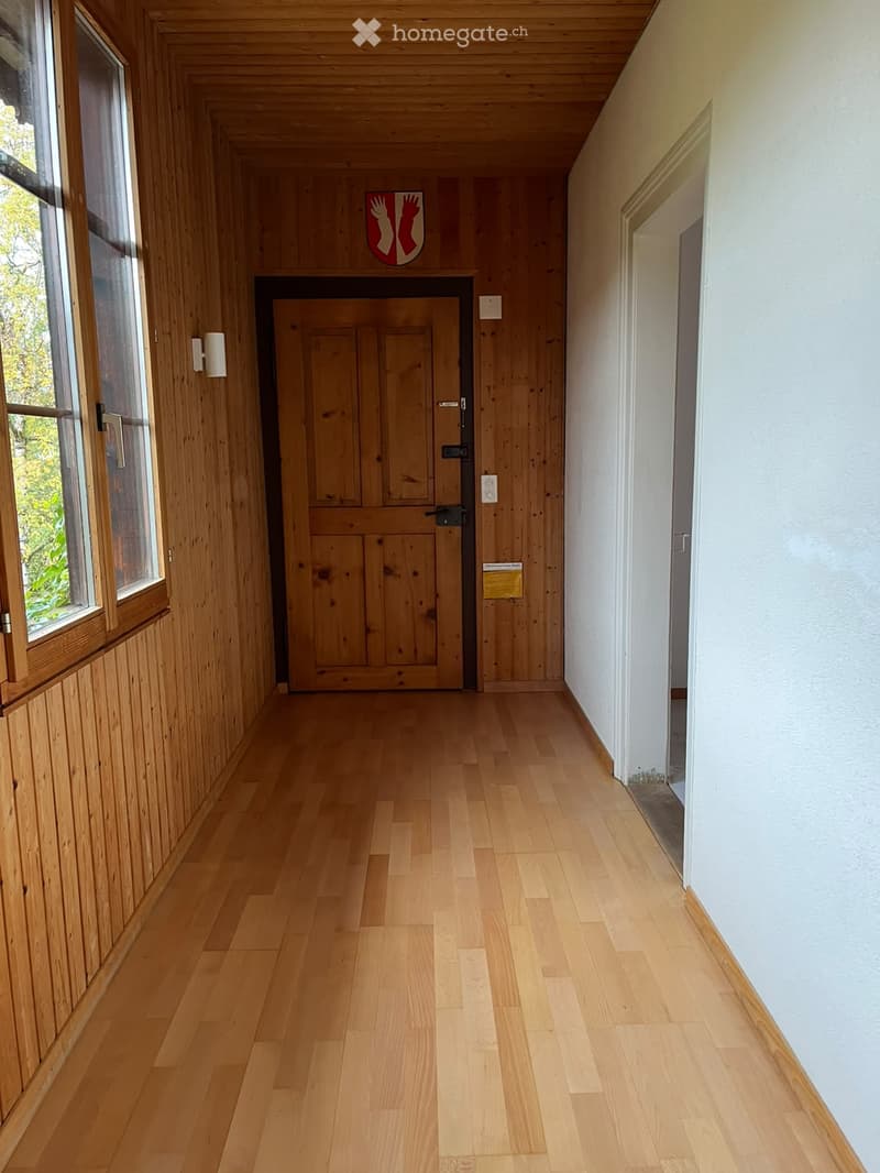 Wooden hallway with light-colored wooden flooring, white walls, and a wooden door at the end.