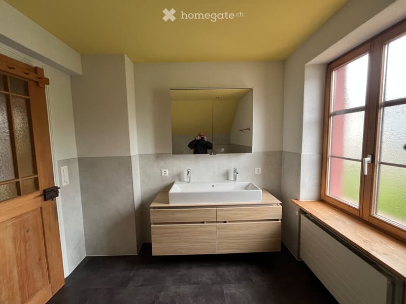Modern bathroom with a double sink, wooden cabinet, large mirror, and frosted glass window.