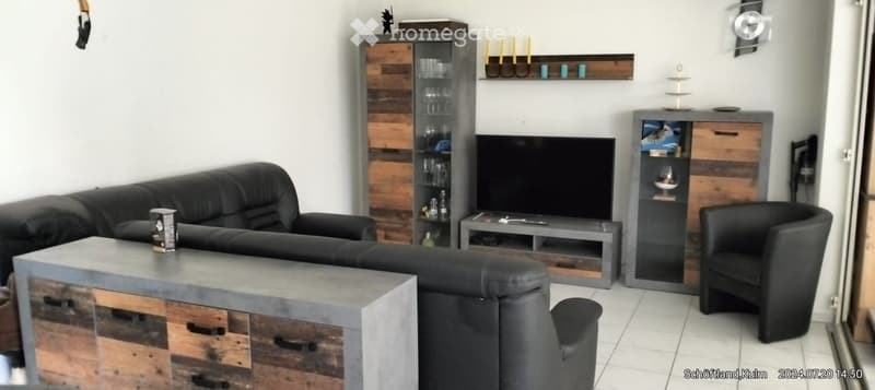 Modern living room with a black leather sofa, armchair, coffee table, TV stand, and wooden cabinets.