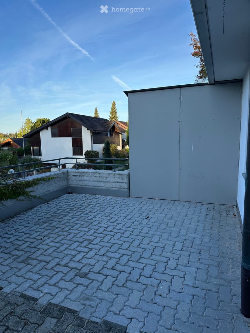 Balcony with a paved stone floor, metal railing, and a view of neighboring houses and greenery.