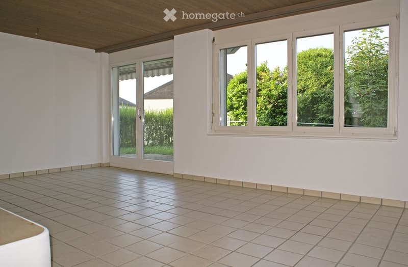 Empty room with tiled floor, white walls, large windows, and a wooden ceiling.