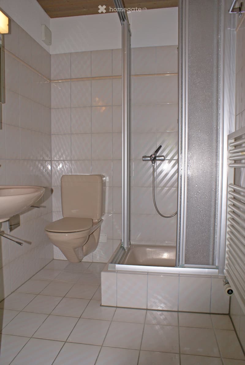 A small bathroom with beige tiles, a toilet, a sink, and a shower with a glass enclosure.