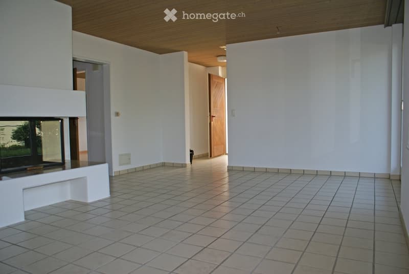 Empty hallway with tiled floor, white walls, and a fireplace on the left side. The hallway leads to another room with a wooden door.